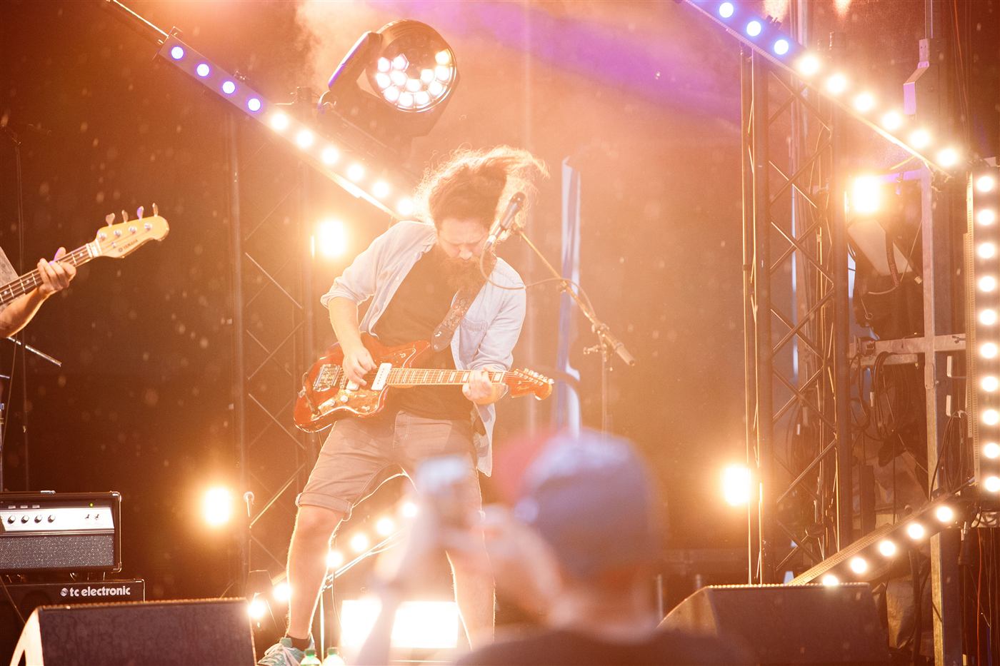Guitarist on an open-air stage framed by festival lights